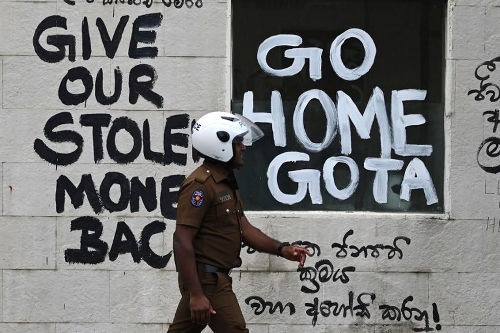 Seorang polisi berjalan melewati sebuah slogan di dinding tembok di Colombo, 21 Juli 2022, yang intinya bernada melawan Presiden Sri Lanka yang baru terpilih Ranil Wickramasinghe. Tembok tersebut terdapat di dekat kediaman kantor presiden di Colombo.