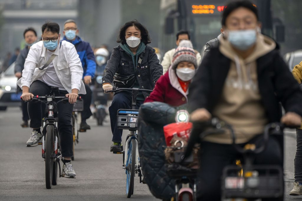 Para komuter yang mengenakan masker mengendarai sepeda di sepanjang jalan di kawasan pusat bisnis di Beijing, China, 20 Oktober 2022.