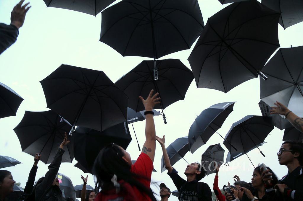 Peserta aksi melempar payung hitam ke atas dalam Aksi Kamisan Ke-500 di seberang Istana Merdeka, Jakarta, Kamis (27/7/2017). 