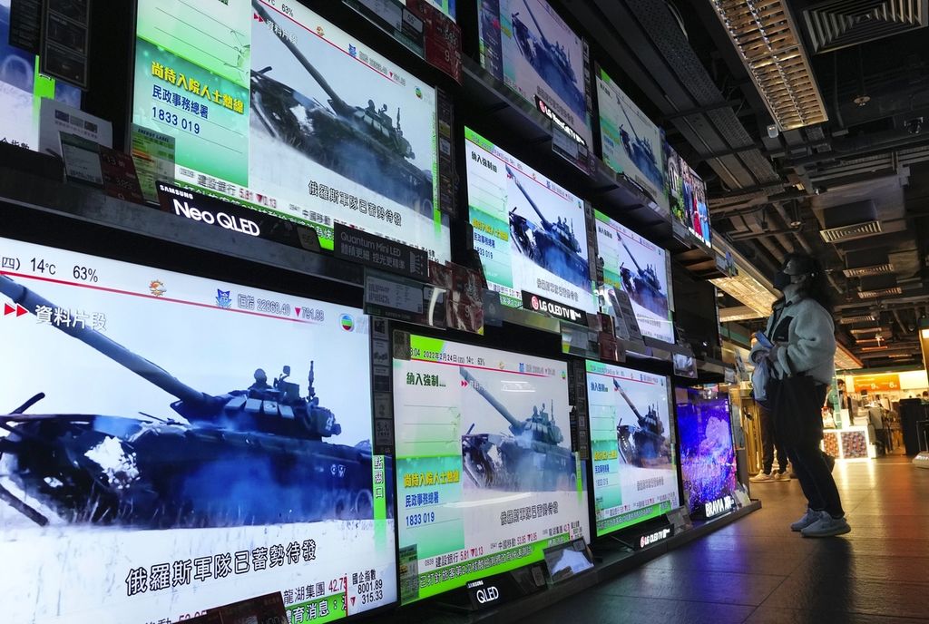 Seorang warga Hong Kong tengah menyaksikan siaran televisi yang memperlihatkan tentara Rusia menggelar serangan ke Ukraina, Kamis (24/2/2022), di sebuah mal di Hong Kong. 