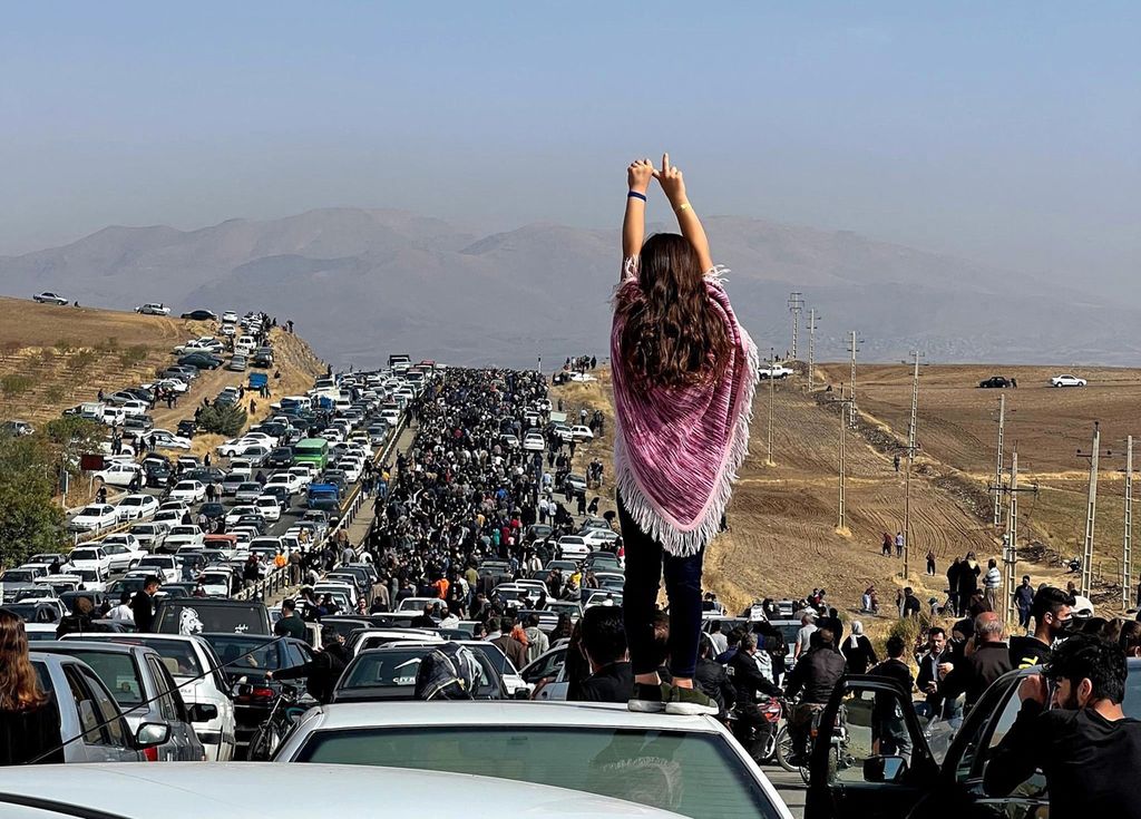 Gambar UGC yang di-<i>posting</i> di Twitter ini dilaporkan pada 26 Oktober 2022 menunjukkan seorang wanita tak bercadar berdiri di atas kendaraan saat ribuan orang berjalan menuju pemakaman Aichi di Saqez, kampung halaman Mahsa Amini di Provinsi Kurdistan, Iran barat, untuk menandai 40 hari sejak kematiannya, menentang langkah-langkah keamanan yang ditingkatkan sebagai bagian dari tindakan keras berdarah terhadap protes yang dipimpin perempuan. Gelombang kerusuhan telah mengguncang Iran sejak Amini yang berusia 22 tahun meninggal pada 16 September, menyusul penangkapannya oleh polisi moralitas di Teheran karena diduga melanggar aturan ketat negara tentang jilbab dan pakaian sederhana. 
