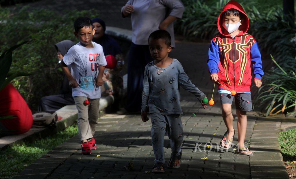 Anak-anak membawa mainan lato-lato saat berkunjung bersama keluarga mereka di Taman Ayodya, Kebayoran Baru, Jakarta Selatan, Minggu (1/1/2023). 