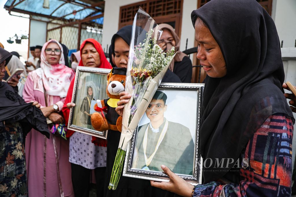 Kerabat menangis sembari membawa foto korban kecelakaan bus di Subang, Dimas Aditya (kanan) dan Intan Rahmawati (kiri), di sekitar rumah duka di Depok, Jawa Barat, Minggu (12/5/2024).