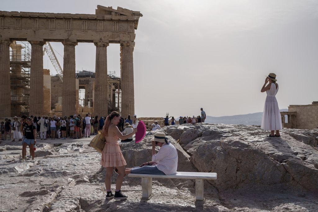 Turis menggunakan kipas angin tangan untuk mendinginkan temannya di Parthenon, kompleks kuno Acropolis, Athena, Yunani, Rabu (12/6/2024). 