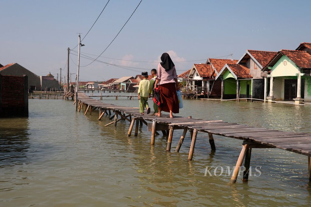 Orangtua bersama anaknya melalui jembatan setelah akses jalan berubah menjadi genangan laut di Desa Timbulsloko, Kecamatan Sayung, Kabupaten Demak, Jawa Tengah, Rabu (29/5/2024). 