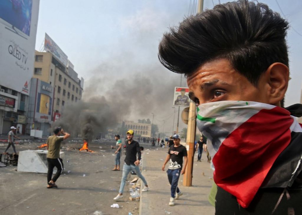 Foto dokumentasi yang menunjukkan seorang pengunjuk rasa mengenakan bendera nasional Irak sebagai masker. Ia berdiri selama bentrokan antara pengunjuk rasa dan polisi antihuru hara di tengah demonstrasi menentang korupsi negara, kegagalan layanan publik, dan pengangguran, di Lapangan Tahrir pusat ibu kota Irak, Baghdad pada Oktober 3, 2019. 