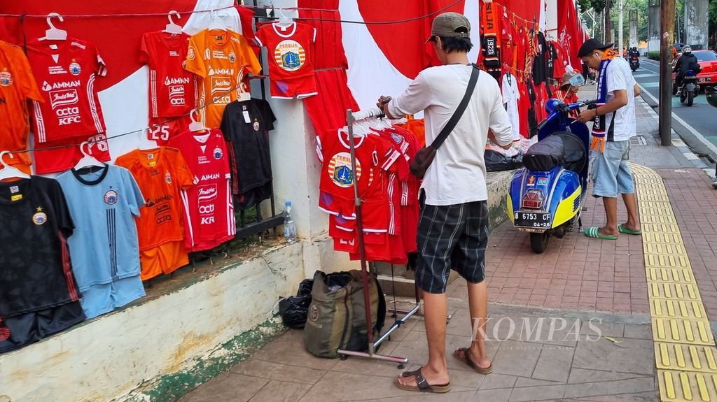 Seorang pedagang membenahi barang jualan yang merupakan jersei ”KW” Persija Jakarta di trotoar Kompleks Parlemen, Jakarta, Minggu (30/7/2023). 