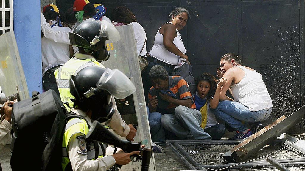 Demonstran anti pemerintah  berlindung saat pasukan anti huru-hara Bolivarian bergerak maju dalam unjuk rasa di Caracas, Venezuela, Rabu (19/4). Kubu oposisi menyerukan massa untuk turun ke jalan menentang kepemimpinan Presiden Venezuela Nicolas Maduro. Unjuk rasa selama beberapa waktu terakhir menyebabkan sejumlah pengunjuk rasa tewas.