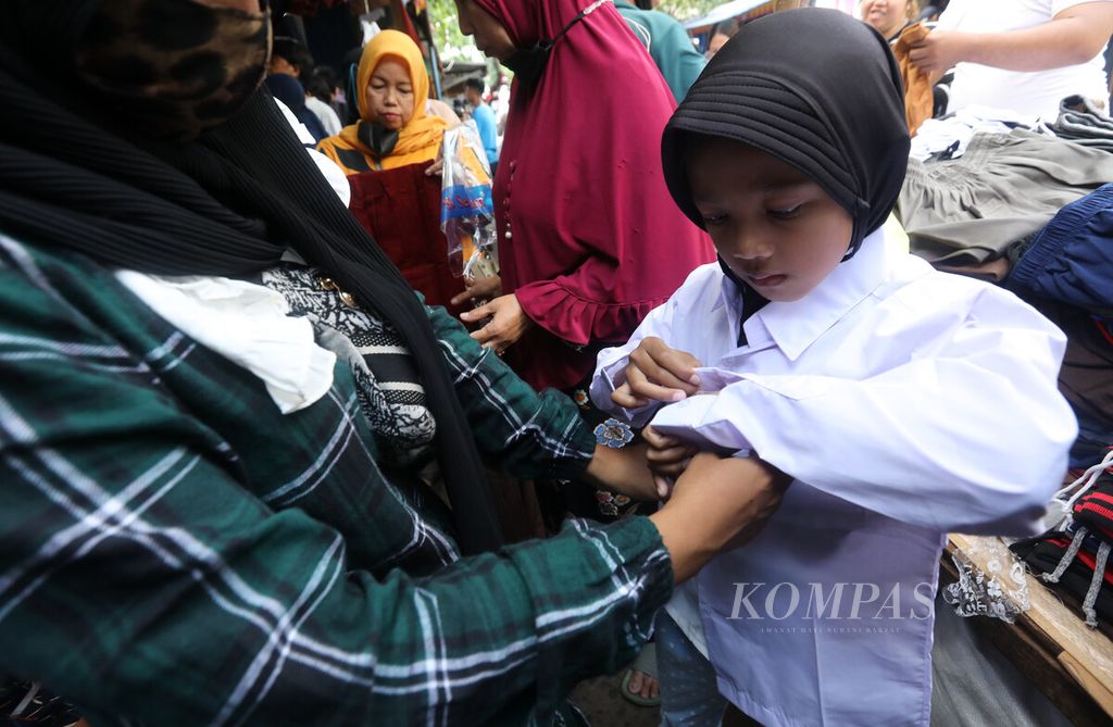 Seorang anak mencoba baju seragam saat ditemani orangtuanya berbelanja kebutuhan sekolah di satu lapak pedagang di Pasar Jatinegara, Jakarta, Minggu (10/7/2022). 
