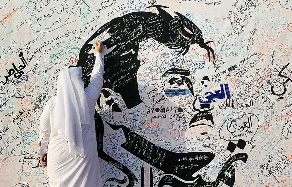 Seorang pria menulis pesan di dinding bergambar Emir Qatar Sheikh Tamim bin Hamad al-Thani di Doha, Minggu (2/7). 
