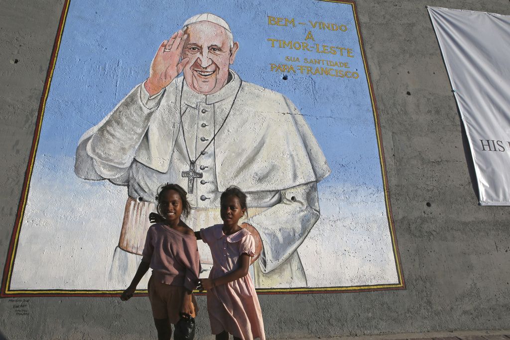 Dua anak perempuan berdiri di depan foto gambar Paus Fransiskus yang dipasang untuk menyambut kedatangan Paus Fransiskus di Dili, Timor Leste, Selasa (4/9/2024). 