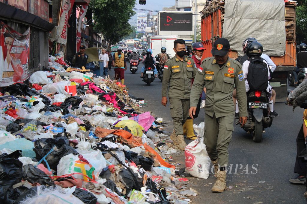 Sejumlah petugas satuan perlindungan masyarakat (linmas) melewati tumpukan sampah di ruas Jalan Ahmad Yani, dekat Pasar Cicadas, Kota Bandung, Jawa Barat, Selasa (7/11/2023). Banyaknya warga yang membuang sampah di pinggir jalan ini membuat petugas perlu berjaga di sejumlah lokasi.