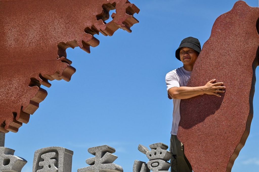 Seorang turis berpose di monumen yang mewakili daratan China (kiri) dan Taiwan (kanan) di Pulau Pingtan, Provinsi Fujian, China, 6 Agustus 2022. Tampak seorang turis memeluk monumen Taiwan. 