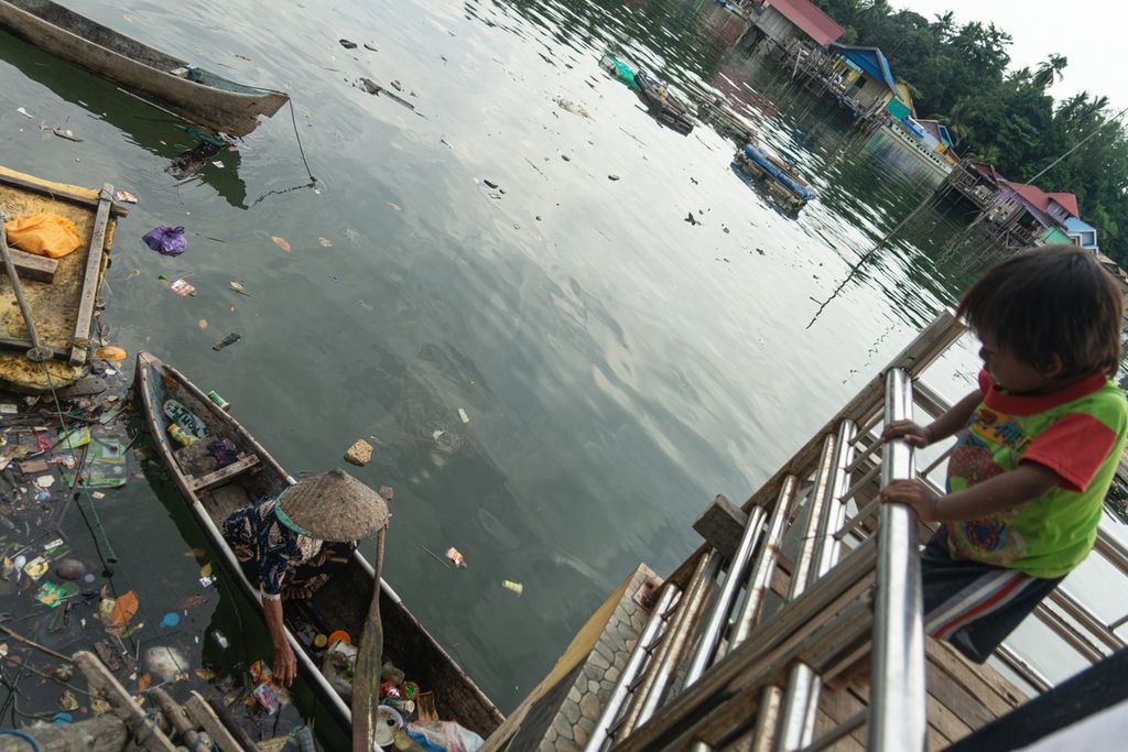 Hanafiah memulung sampah plastik di pesisir Teluk Kendari, Sulawesi Tenggara, disaksikan cucunya, Minggu (2/1/2022).