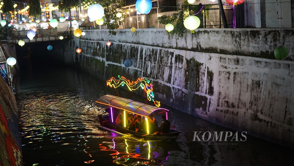 Perahu berhiaskan lampu warna-warni melintasi Kali Pepe dalam Grebeg Sudiro di Kota Surakarta, Jawa Tengah, Senin (16/1/2023) malam. Keberadaan wisata perahu membangkitkan ingatan tentang kejayaan jalur transportasi air di kota tersebut pada masa lampau.