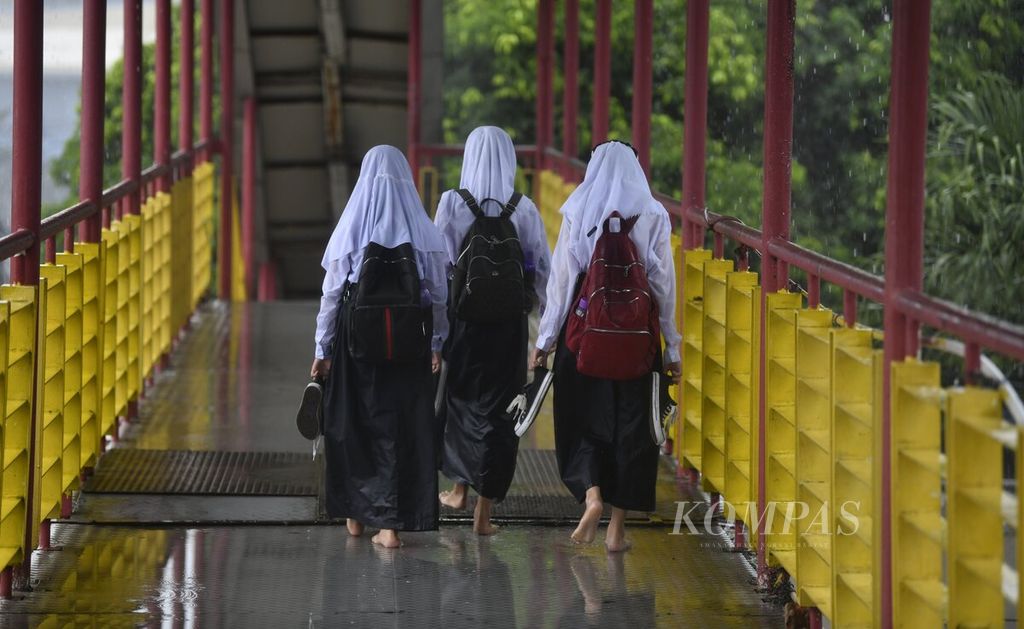 Sejumlah pelajar menenteng sepatu yang basah karena hujan saat pulang sekolah di kawasan Gambir, Jakarta, saat hujan deras mengguyur, Selasa (18/1/2022).