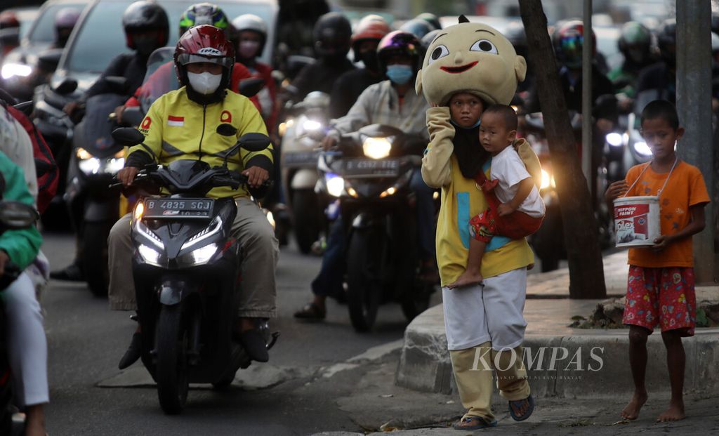 Remaja menggendong anak balita sembari mengamen mengenakan baju badut berkelana di jalan di kawasan Gatot Subroto, Jakarta Selatan, di tengah arus kemacetan lalu lintas pada jam pulang kerja, Kamis (7/4/2022). Kemiskinan membawa anak-anak turun ke jalan mencari tambahan penghasilan untuk menopang hidup mereka sehari-hari. 