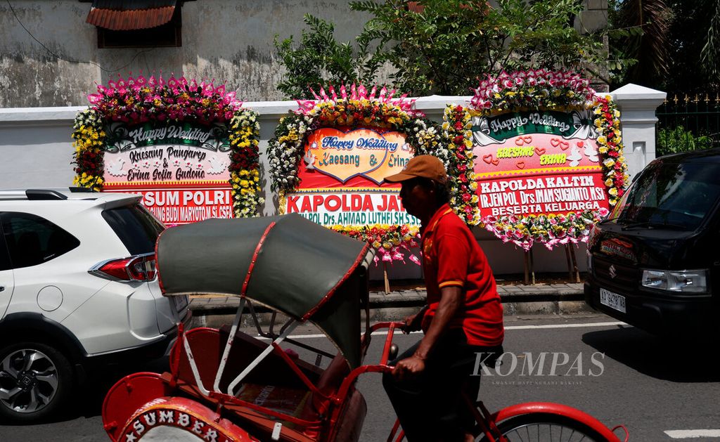 Pengemudi becak melintasi karangan bunga ucapan sukacita untuk pernikahan Kaesang Pangarep-Erina Gudono di Pura Mangkunegaran, Kota Surakarta, Jawa Tengah, Sabtu (10/12/2022). 