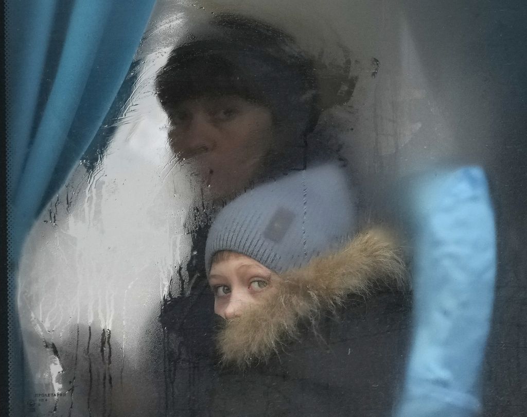 Seorang wanita dan anak mengintip dari jendela bus saat mereka meninggalkan Sievierodonetsk, wilayah Luhansk, di timur Ukraina, Kamis, 24 Februari 2022.