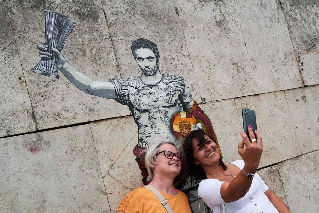 Dua perempuan berswafoto di depan lukisan mural Pelatih AS Roma Jose Mourinho yang dibuat Harry Greb, Kamis (26/5/2022). Lukisan yang menyerupai sosok gladiator Roma itu merupakan bentuk penghormatan atas Mourinho yang membawa AS Roma menjuarai Liga Konferensi Eropa musim 2021-2022.