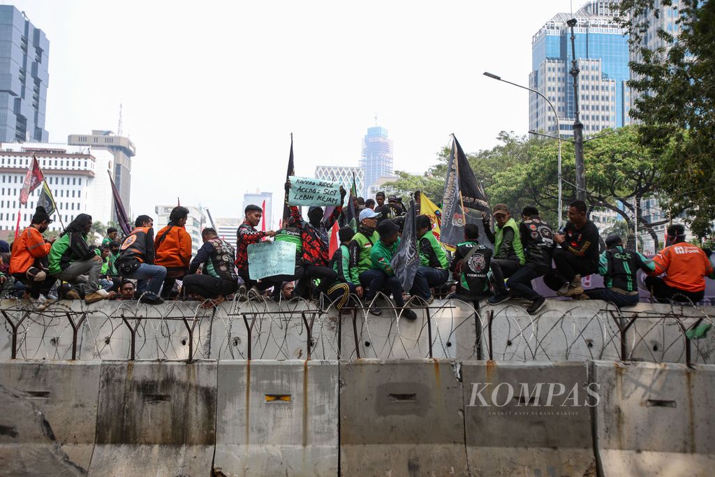 Para pengemudi ojek <i>online</i> atau ojek daring membentangkan poster berisi tuntutan mereka saat melakukan unjuk rasa di kawasan Patung Kuda Wijaya, Jakarta, Kamis (29/8/2024).