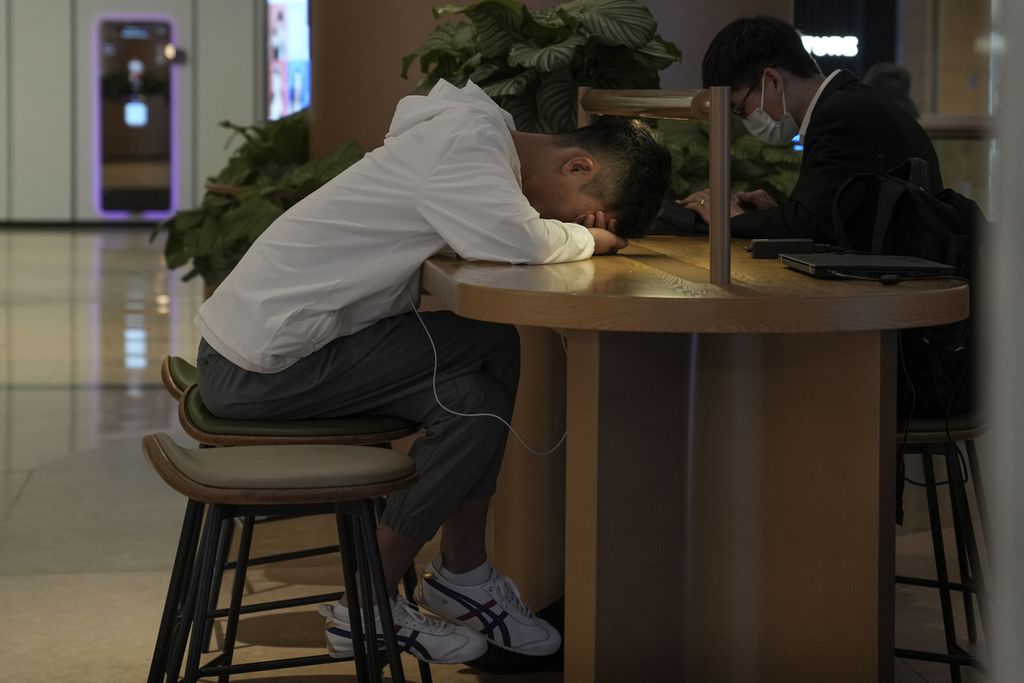 Seorang laki-laki tidur siang di samping komputer di sebuah kafe di Beijing, China, pada 24 Mei 2023.