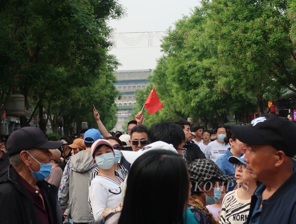 Tampak seorang warga mengayunkan bendera China di antara lautan warga yang memadati kawasan Qianmen Street, Beijing, China, Senin (1/5/2023). Mereka merayakan hari buruh dengan berwisata bersama keluarga, teman dekat, dan pasangan. Qianmen Street adalah sebuah jalan pedestrian dengan sejarah lebih dari 500 tahun yang terkenal sebagai area berbelanja bernuansa China tempo dulu.