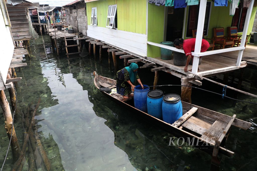 Warga mengalirkan air dari saluran PDAM ke dalam tong di rumah salah satu warga di Kampung Bajo Torosiaje, Kabupaten Pohuwato, Gorontalo, Jumat (15/7/2022).