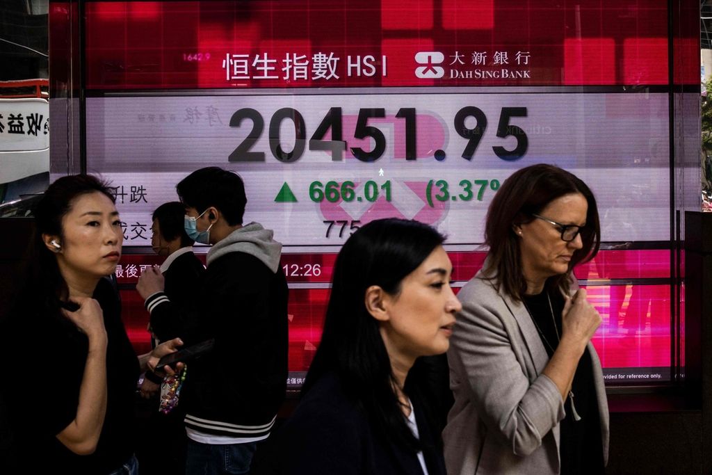 Para pekerja berjalan melintasi layar elektronik yang menunjukkan Hang Seng Index di Hong Kong, 1 Maret 2023. Otoritas Hong Kong mencabut aturan wajib bermasker sejak 1 Maret 2023. 