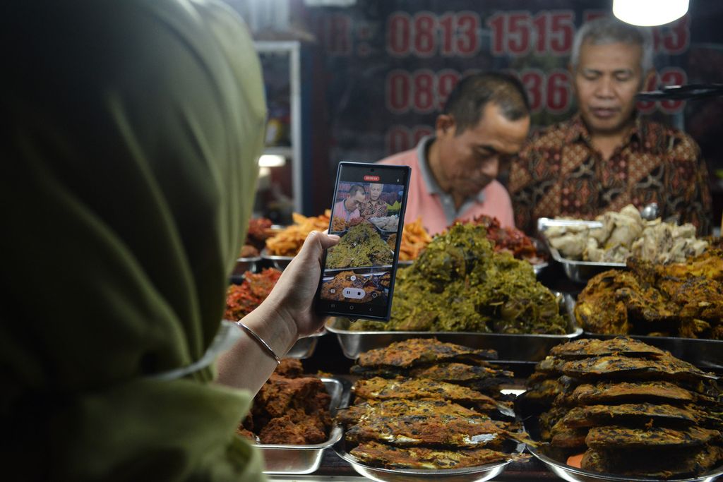 Salah satu pembeli merekam pedagang menyiapkan sajian nasi kapau di kawasan kuliner Jalan Kramat Raya, Jakarta Pusat, Jumat (14/4/2023). 