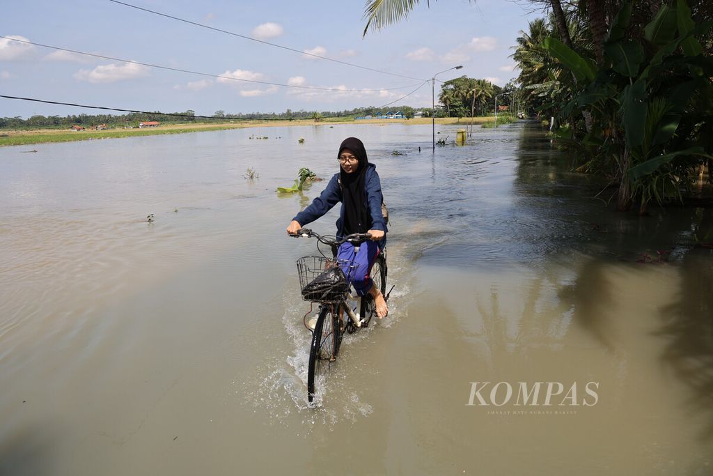 Warga melintasi banjir di jalanan di kawasan permukiman  Desa Sidomulyo, Butuh, Purworejo, Jawa Tengah, Rabu (16/3/2022). 