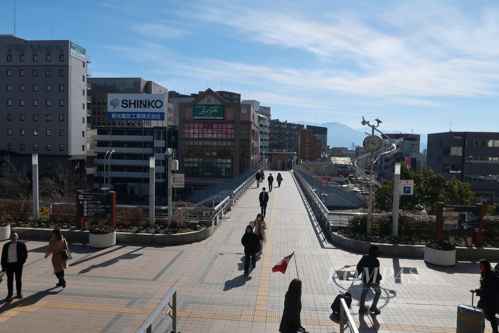 Penumpang kereta berjalan keluar dan masuk Stasiun Nagano di Nagano, Jepang, Jumat (17/2/2023). Tampak pula pemandangan kota Nagano di kejauhan yang dikelilingi Pegunungan Alpen Utara.