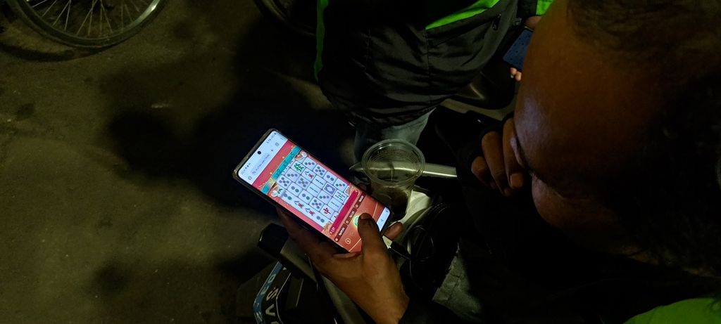 Seorang pengojek membuka situs judi slot dari ponsel di sekitar jembatan layang di Pancoran, Jakarta Selatan, Senin (20/11/2023). 