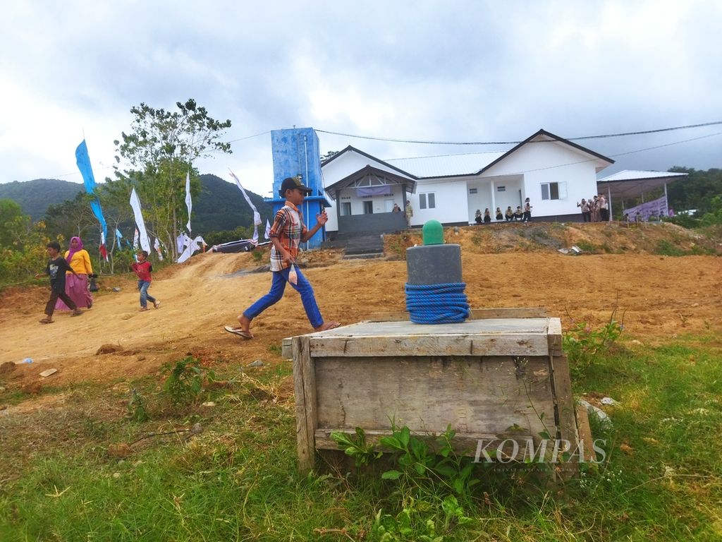 Warga melintas di sumur air bersih dengan latar belakang tandon air (warna biru) dan bangunan AFC Health Center Puskesmas Plus Bakti Nusantara Aik Mual, Desa Sekotong Timur, Lombok Barat, Nusa Tenggara Barat, Minggu (26/6/2022), 