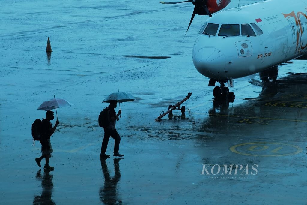 Penumpang menggunakan payung ketika hendak naik ke pesawat saat hujan deras mengguyur kawasan Bandara Internasional Lombok, Nusa Tenggara Barat, Jumat (8/1/2021). Sepanjang 2020, jumlah penumpang di Bandara Internasional Lombok mencapai 1,28 juta orang atau turun sekitar 55,8 persen dari tahun 2019 yang mencapai 2,9 juta penumpang. Penurunan itu akibat merebaknya pandemi Covid-19.