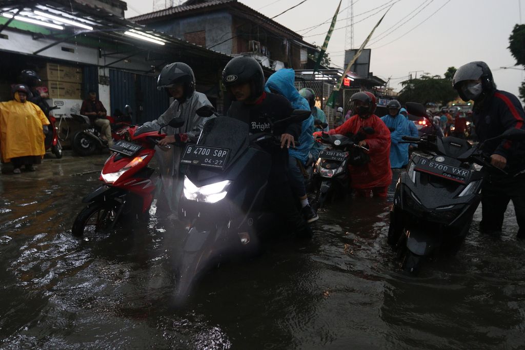 Warga menuntun sepeda motor di tengah banjir di Jalan H Naba Raya, Karang Tengah, Tangerang, Banten, Kamis (13/10/2022). 