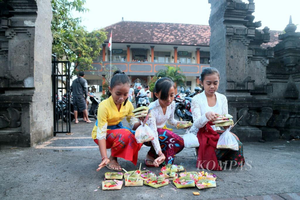 Siswa SD Negeri Kerobokan Kelod 1 menaruh canang (perlengkapan berdoa umat Hindu) di gerbang sekolah mereka di Kawasan Kerobokan Kelod, Badung, Bali, sebelum mengikuti doa bersama di halaman sekolah, Kamis (12/7/2018).