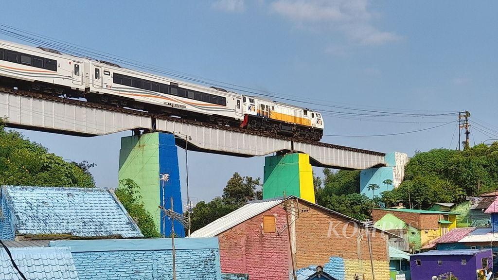 Kereta api yang baru keluar dari Stasiun Malang melintas di atas kampung aneka warna, yakni Kampung Tiga Dimensi/Tridi dan Warna-Warni, di Kecamatan Blimbing, Kota Malang, Jawa Timur, Sabtu (9/7/2022).