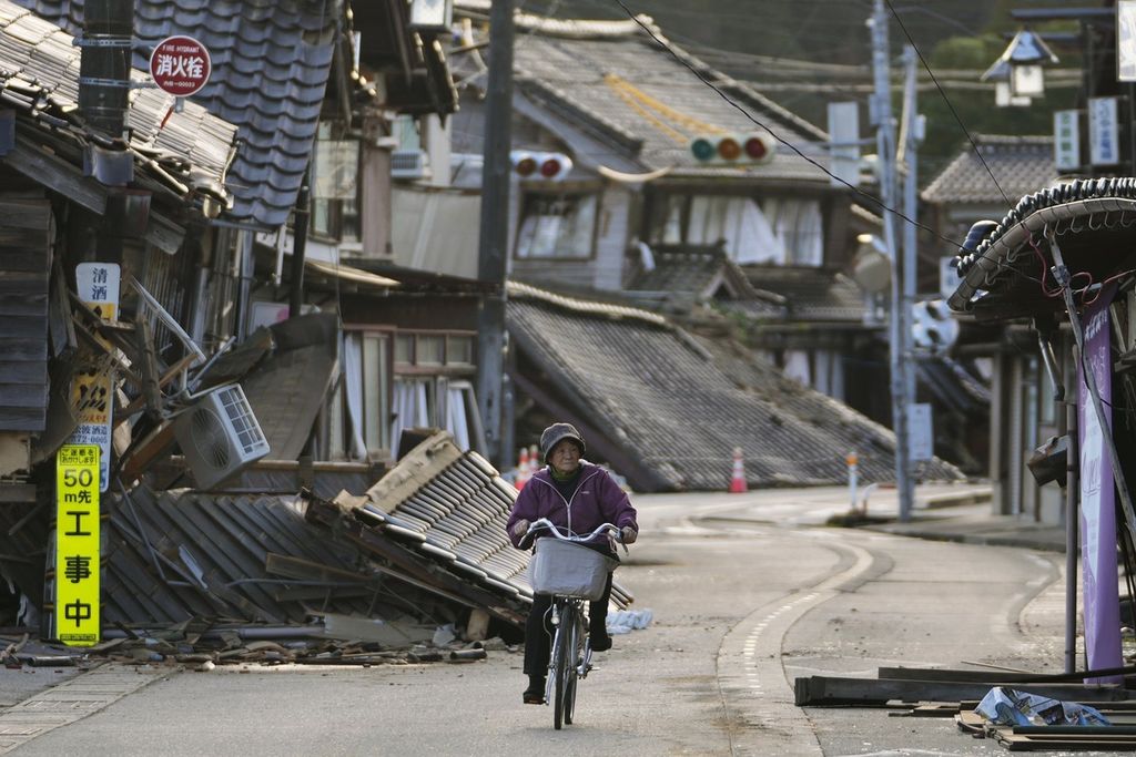 Seorang perempuan warga kota Noto di Semenanjung Noto, Jepang, Selasa (2/1/2024) , mengayuh sepedanya melintasi bangunan yang roboh akibat gempa berkekuatan M 7,6 yang terjadi pada Senin (1/1/2023). Hingga Selasa petang, regu penyelamat mengonfirmasi, 48 warga meninggal dunia akibat gempa tersebut.  