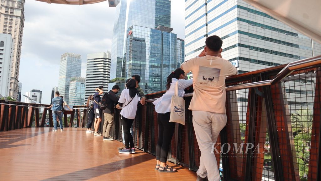 Pengunjung menikmati pemandangan gedung perkantoran dari lantai dua anjungan pandang jembatan penyeberangan orang Pinisi di Jalan Sudirman, Jakarta Pusat, Rabu (6/4/2022) sore.