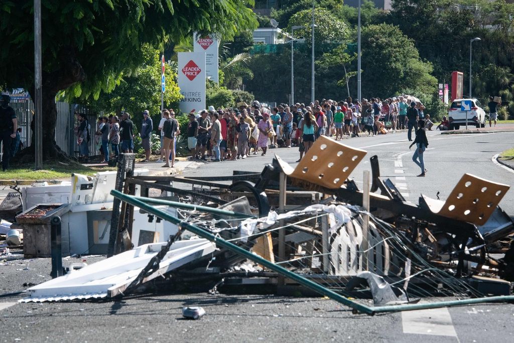 Orang-orang mengantre untuk membeli perbekalan dari toserba di sepanjang jalan yang ditutup oleh puing-puing dan barang-barang yang terbakar menyusul kerusuhan semalam di distrik Magenta di Noumea, wilayah Pasifik Perancis di Kaledonia Baru, pada 18 Mei 2024. 