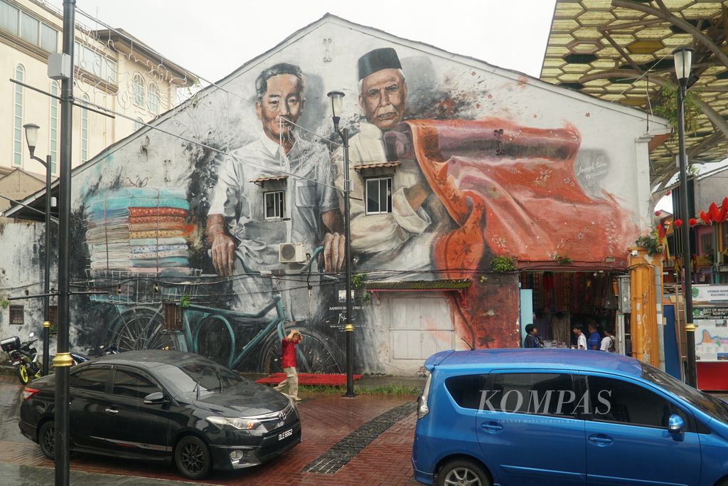 Seorang pria berjalan di bawah mural ”The Early Merces” di dekat akses masuk Jalan India, kota Kuching, Sarawak, Malaysia, Kamis (22/2/2024). 
