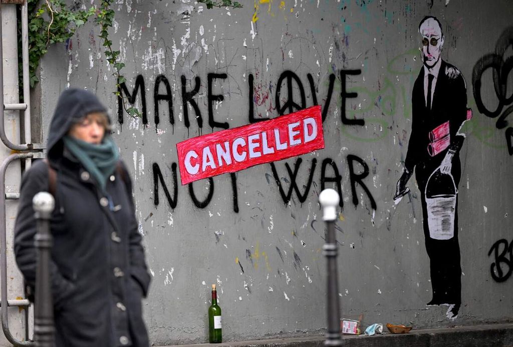 Seorang perempuan berjalan melewati mural yang menggambarkan Presiden Rusia Vladimir Putin dengan tulisan dibatalkan” di atas tulisan ”Make Love Not War”, di Paris, Perancis, Minggu (13/3/2022).