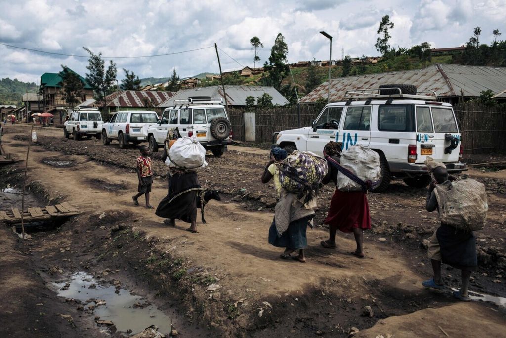 Sejumlah warga kembali ke kota Mweso, Provinsi Kivu Utara, Kongo. Mereka berjalan memikul hasil panen melewati konvoi kendaraan MONUCSO. Foto diambil pada 10 April 2019.