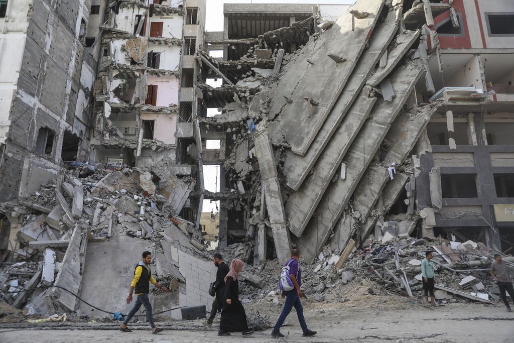 Foto yang diambil pada Jumat (24/11/2023) memperlihatkan beberapa warga Gaza berjalan di depan apartemen yang rusak berat akibat pertempuran antara Hamas dan Israel di kota tersebut. 