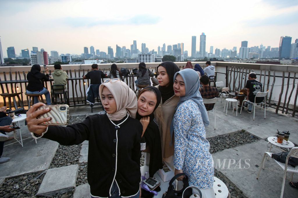 Pengunjung berswafoto dengan latar belakang gedung-gedung tinggi di salah satu kafe di kawasan Tebet, Jakarta Selatan, akhir Juni 2024. 