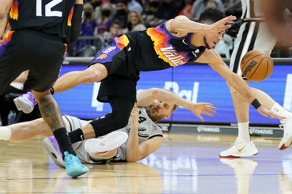 <i>Guard</i> Phoenix Suns, Devin Booker, dan <i>center</i> San Antonio Spurs, Jock Landale, berduel memperebutkan bola dalam pertandingan NBA antara Phoenix Suns dan San Antonio Spurs di Phoenix, Minggu (30/1/2022) waktu setempat.