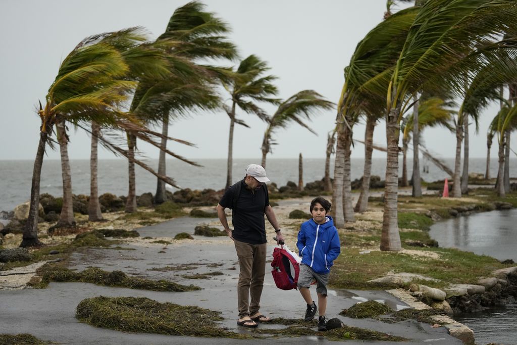Bob Givehchi (kiri) dan putranya, Daniel (8), warga Toronto, Kanada, sedang mengunjungi Miami, Amerika Serikat. Mereka melewati puing-puing dan pohon palem yang tertiup angin kencang di Matheson Hammock Park di Coral Gables, Florida, Jumat (15/12/2023). 