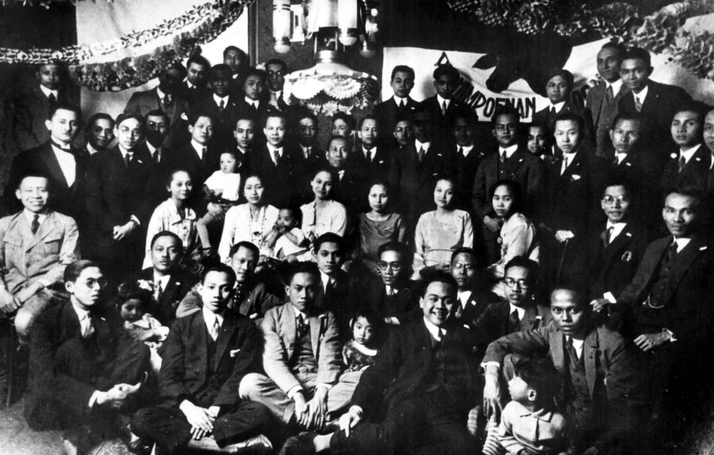 Para anggota Perhimpunan Indonesia (1925) dengan latar belakang bendera Merah Putih. Tampak berdiri (Mr.) Subardjo, Moh. Zain (Mr.) Darsono, (Dr. Mr.) Moh Nazif, (Dr.) Mohammad Hatta, (Mr.) Nazir Pamuntjak, (Dr.) Agustin, (Dr.) Moh Saleh, (Dr.) Slamet, (Dr.) Surono, Dradjat, Djunaidi, (Ir.) Sarsito, (Dr.) Wirasmo, (Dr.) Samsi Sastrowidagdo, (Drs.) Suleiman, (Prof. Dr.) Satochid, (Ir.) Supardi, Sudomo, (Mr.) Husein, (Mr.) Sutikno, (Ir.) Teko, (Prof. Drs) Sukamto Notonegoro. Duduk dari kiri ke kanan: Wajujo, (Dr.) Sumitro, (Prof. Dr. Mr.) Supomo, Sujudi II, (Prof. Mr.) Sunario, (Mr.) Sjarif Hidajat, (Mr.) Budiarto, (Mr.) Karim Pringgodigdo, (Dr.) Abutari, (Prof. Dr. Mr.) Wirjojo Prodjodikoro, (Mr.) Aruman. Juga tampak para istri dokter duduk di tengah.