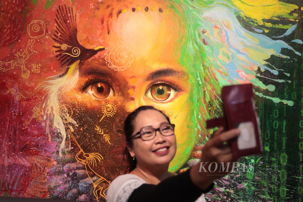 Pengunjung berswafoto dengan latar belakang lukisan karya tujuh perupa yang tergabung dalam Kelompok Tu7uh Rupa dalam pameran Titimangsa di Bentara Budaya Jakarta, Kamis (9/11/2023).